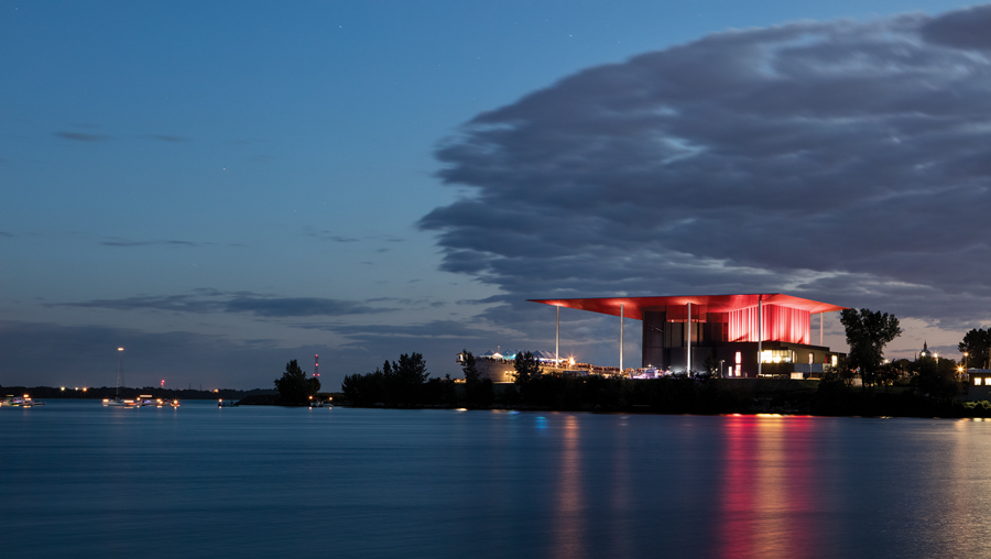 From the water, the red roof of the amphitheatre hovers over the site.