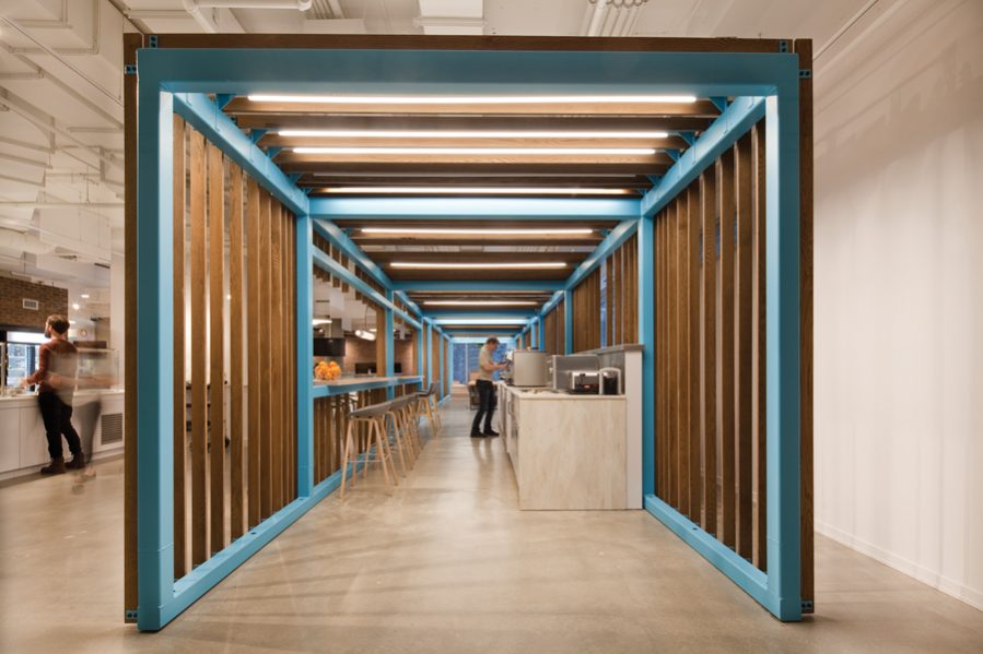 A vibrant blue metal-and-wood scaffold frames an espresso bar and meeting room in Shopify’s Montreal office, lending structure to the open-concept workspace. Photo by Claude-Simon Langlois
