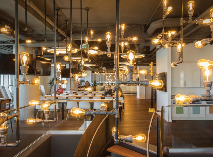 Exposed light bulbs and piping are playfully assembled into industrial-looking luminaires adjacent an employee cafeteria. Photo by Union Eleven