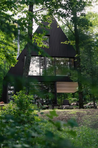 The exaggerated pitch of the roofs and matte black metal siding make the cottage feel like a children's impression of a huge, sheltering spruce tree, rising in the midst of the woods. Photography by Maxime Brouillet
