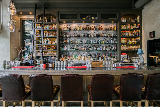 The library inspired bar is the focus of Proof, while a trio of glass and brass clamp lights by Lindsay Adelman are suspended over the leathered black marble bar top.Photo by Phil Crozier, Photophilco.