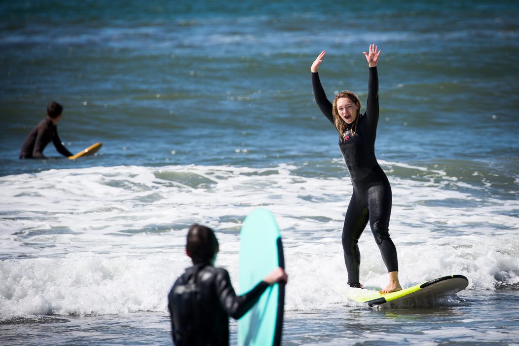 A woman riding into shore on her surf board cheering over her success.