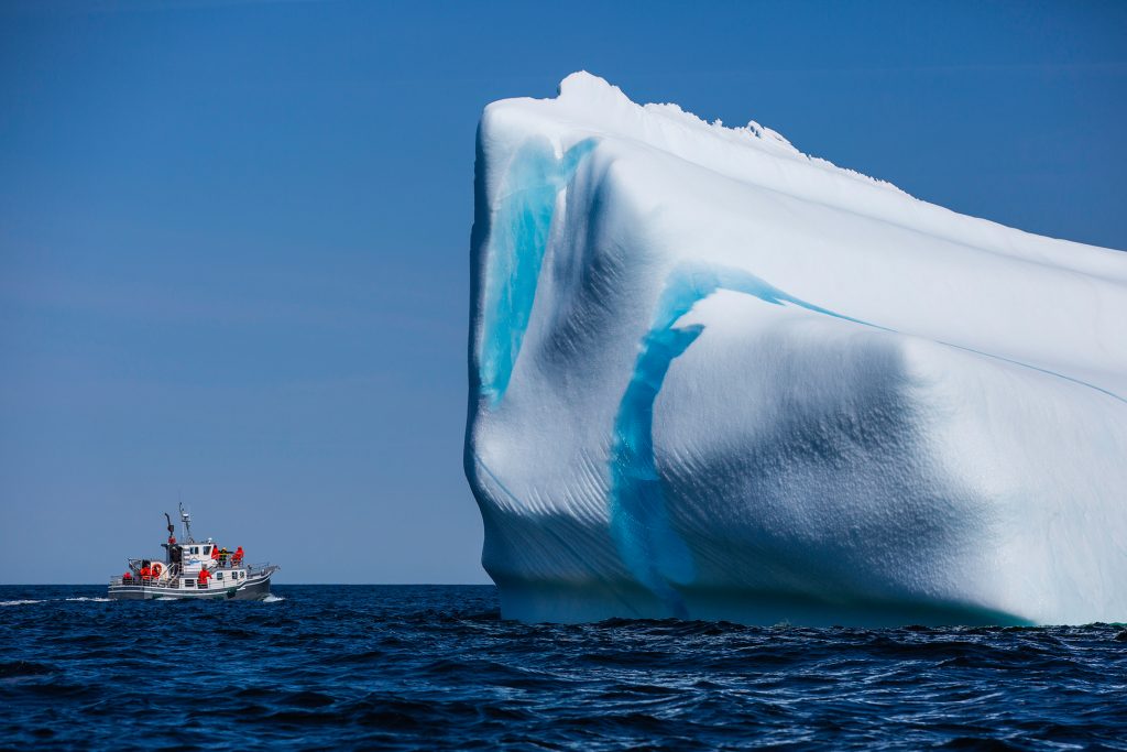 A fishing boat is dwarfed by a large blue and white iceberg
