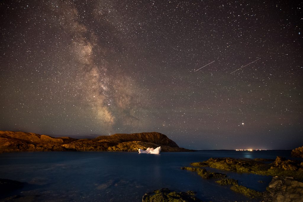 A small iceberg by rocks with the Milky Way above