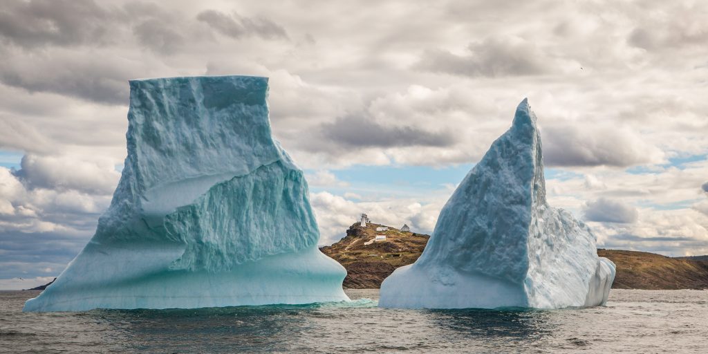 A small fishing village is seen between two halves of a large iceberg at Cape Spear, Newfoundland