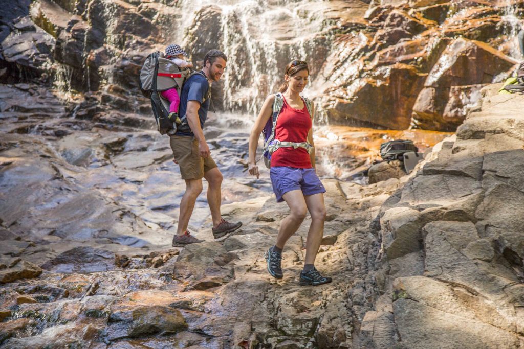 A couple with a baby hiking past a waterfall in Crawford Notch State Park, New Hampshire.
