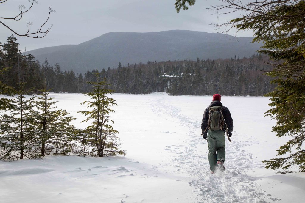 A single person hiking across a snow-covered lake with a view of mountains in New Hampshire