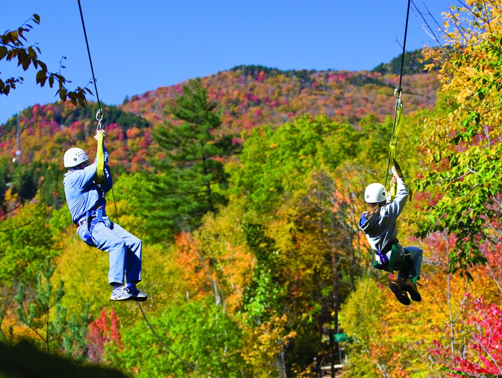 Two people ziplining over mountains with fall colours in New Hampshire