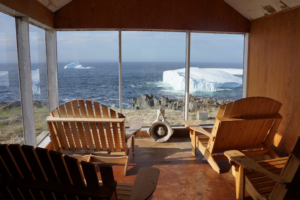 Two wooden muskoka chairs look out over a view of ocean and icebergs