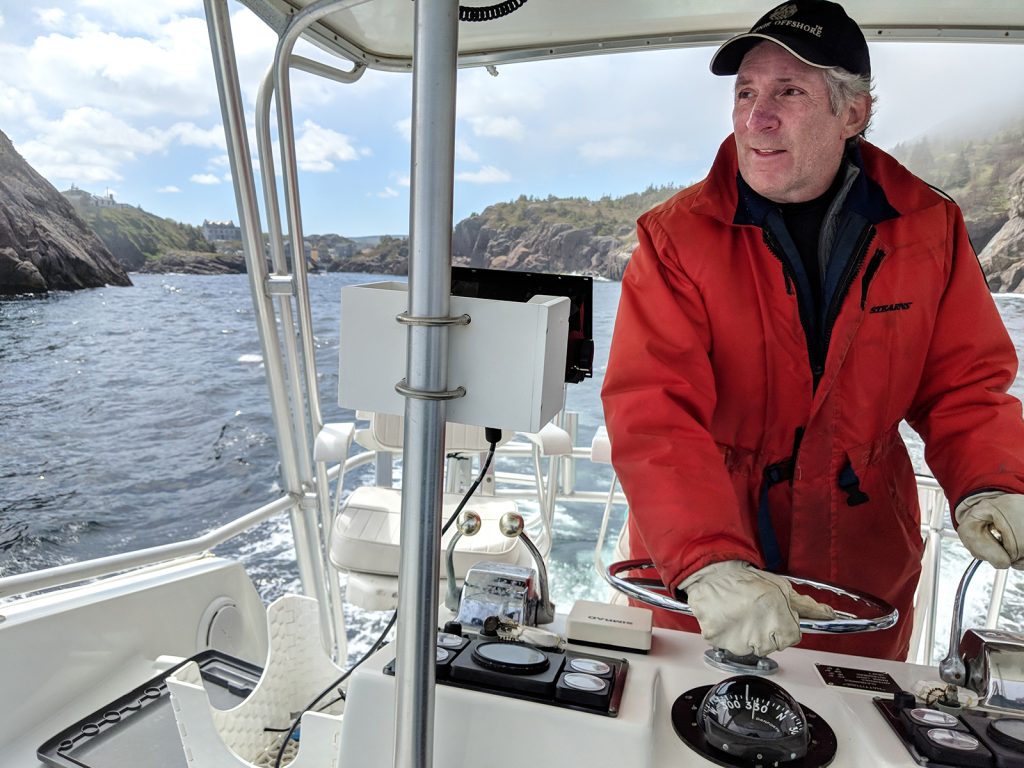 A man in a red raincoat steers a fishing boat through Quidi Vidi Harbour