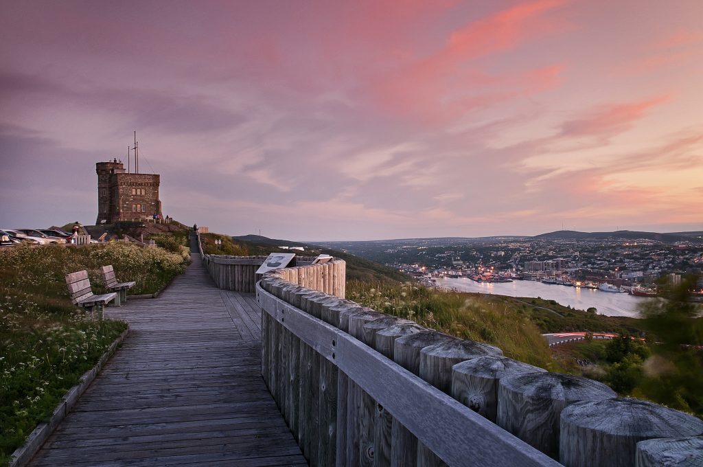 A stone tower atop a hill is almost silhouetted by a pink sunset