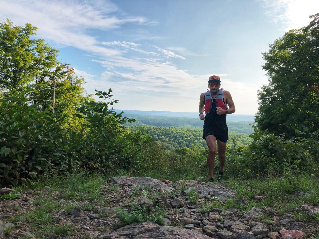 A man runs up a hill with green hills in the background