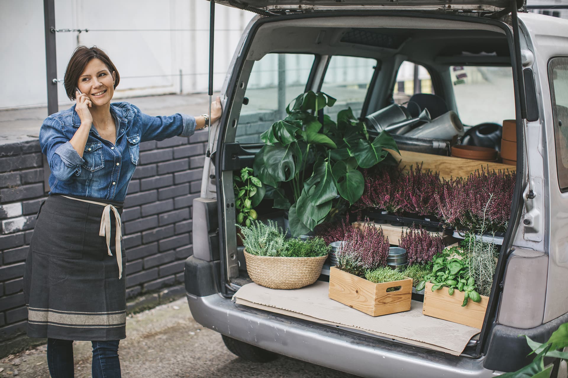 A woman on the phone with plants in the trunk of her car covered by individually rated auto insurance