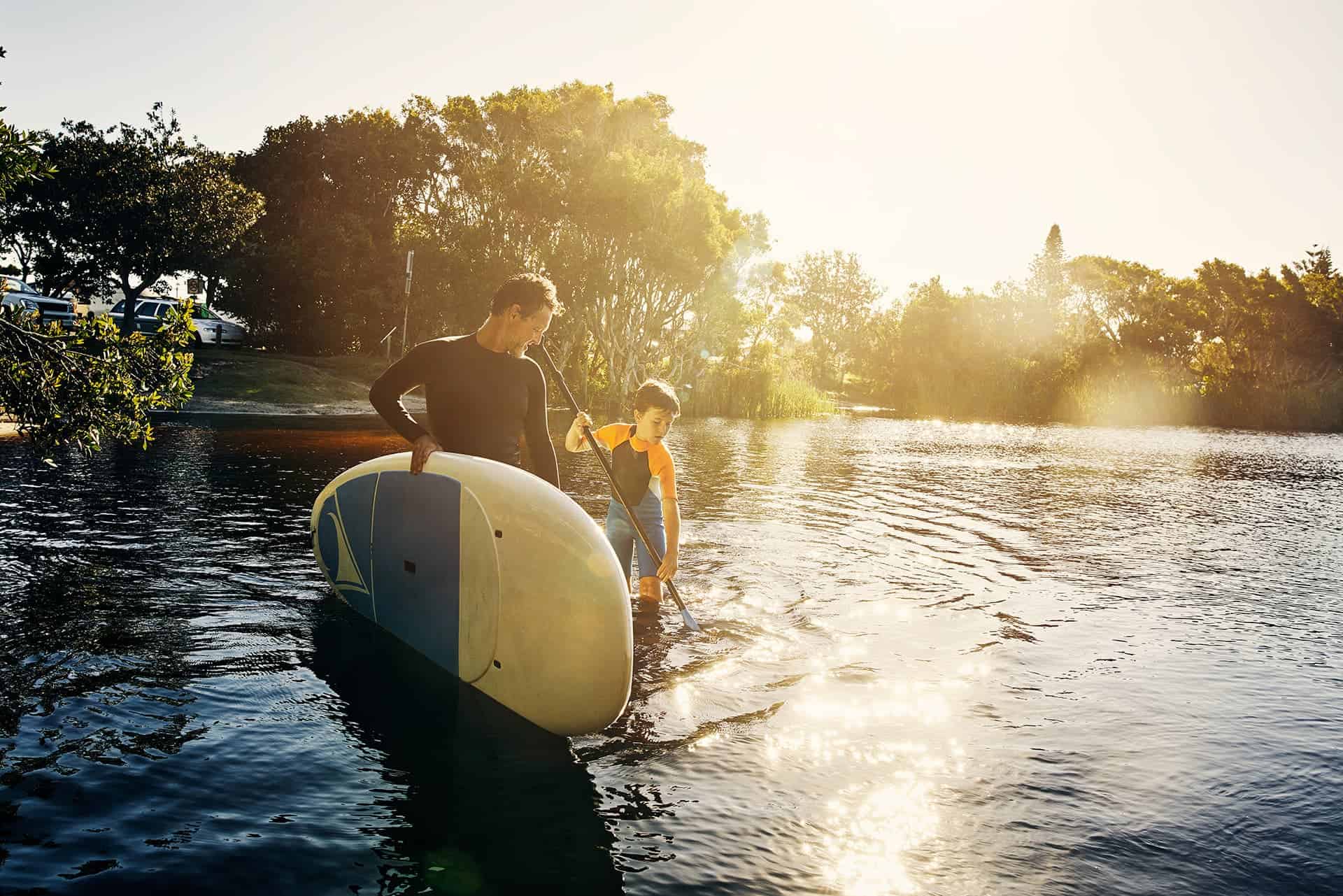 Term life insurance for a father holding a stand up paddle board while his son holds the paddle
