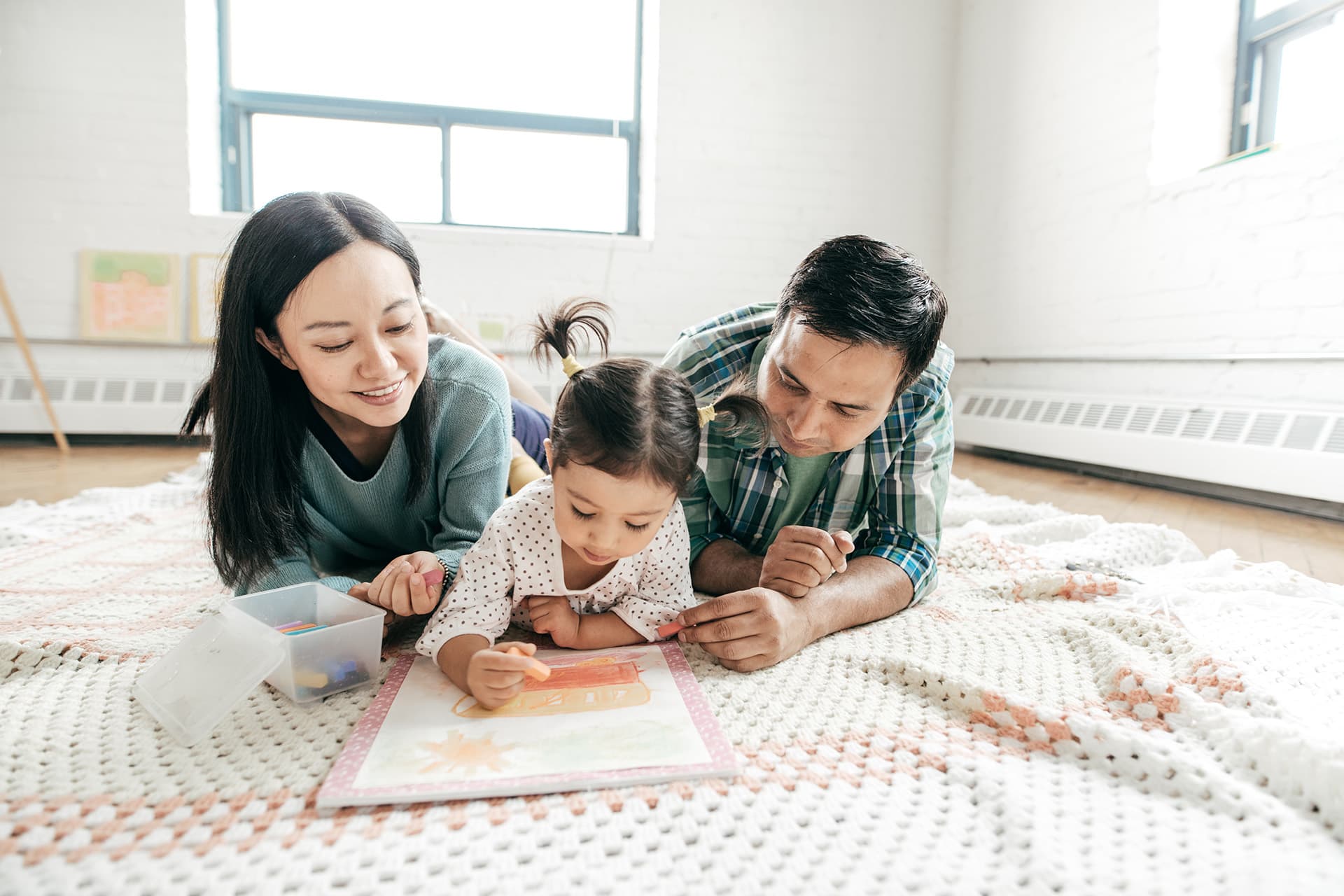 Home insurance for mother and father laying on the ground with their daughter reading a book
