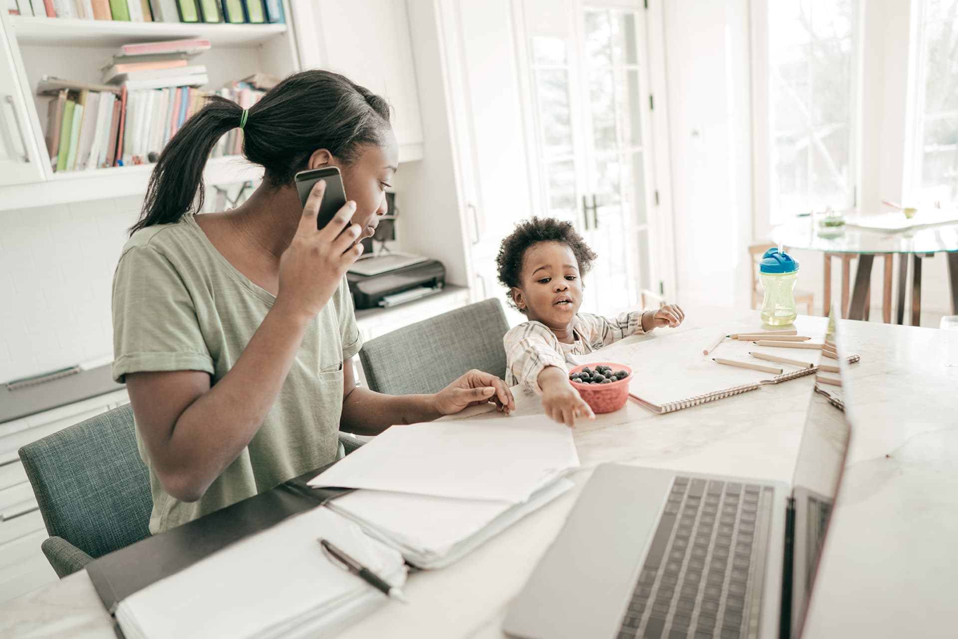 Woman sitting next to her child, talking on the phone, with home business insurance documents in front of her