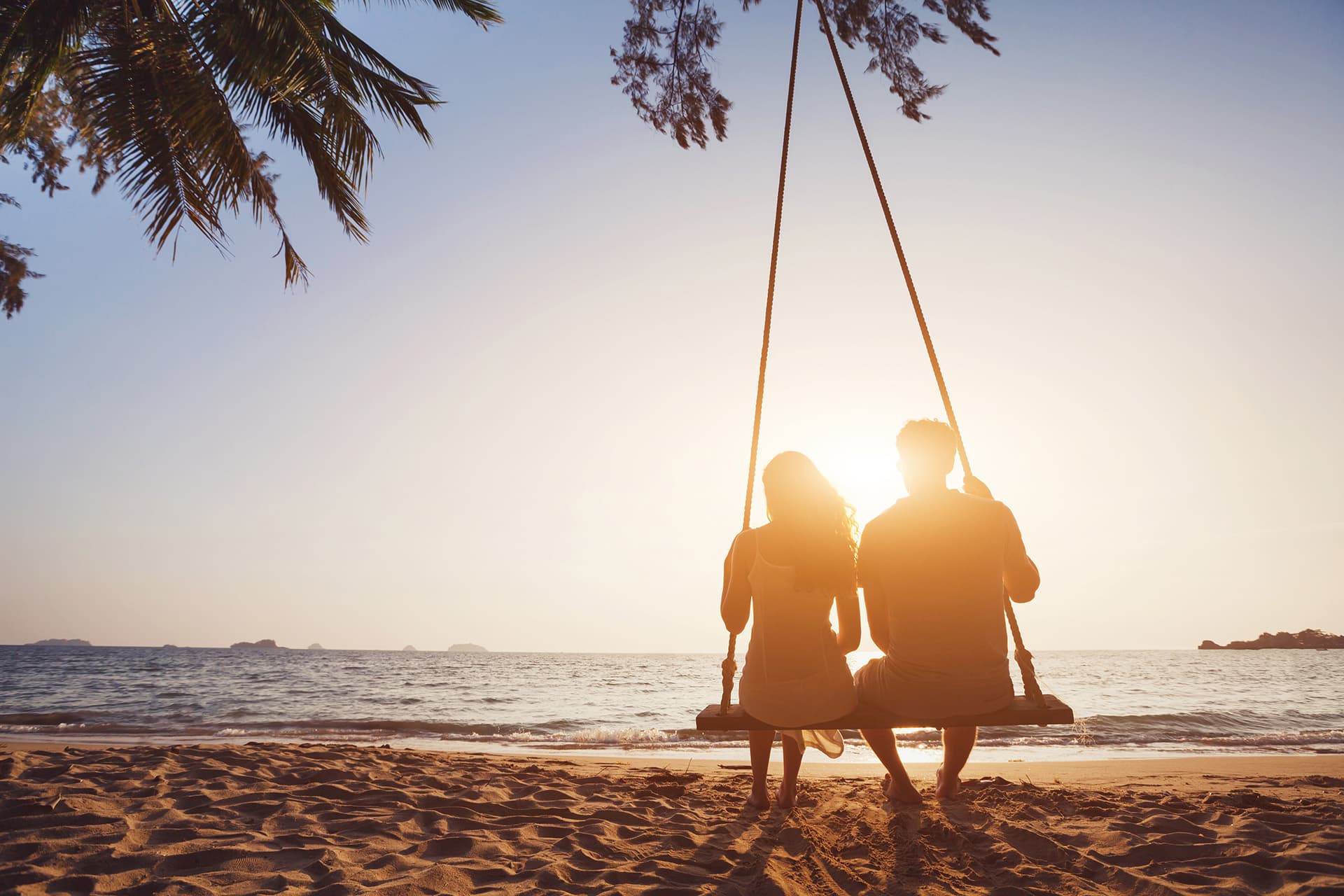 Couple sitting on a swing at a beach with travel insurance