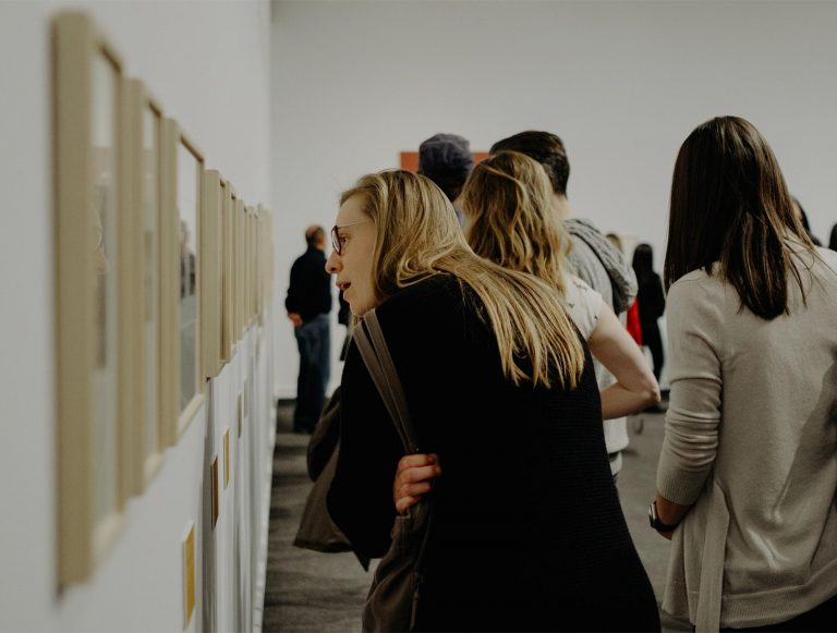 Woman, arms folded, peering at wall of artwork