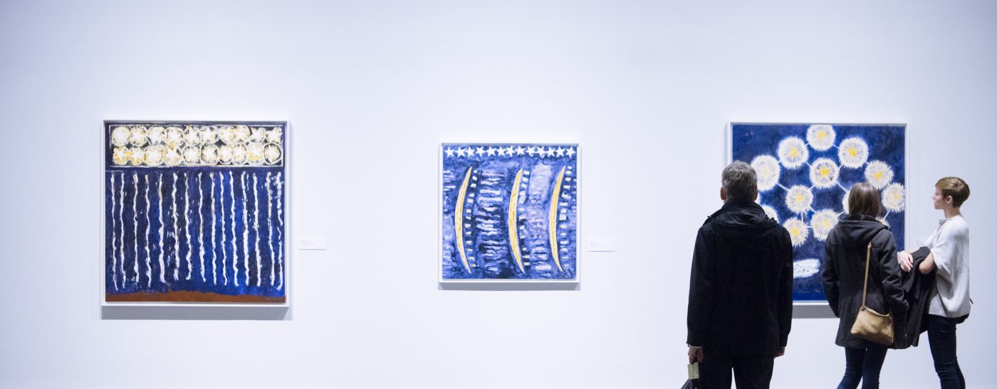 Three people looking at three large blue pieces of art