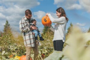 Une mère montre à son jeune enfant, dans les bras de son père, une citrouille fraichement cueillie dans un champ.