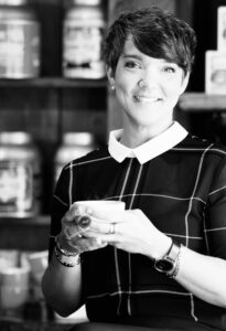 Photo en noir et blanc d'Annie Gaudet, souriante, un café à la main.