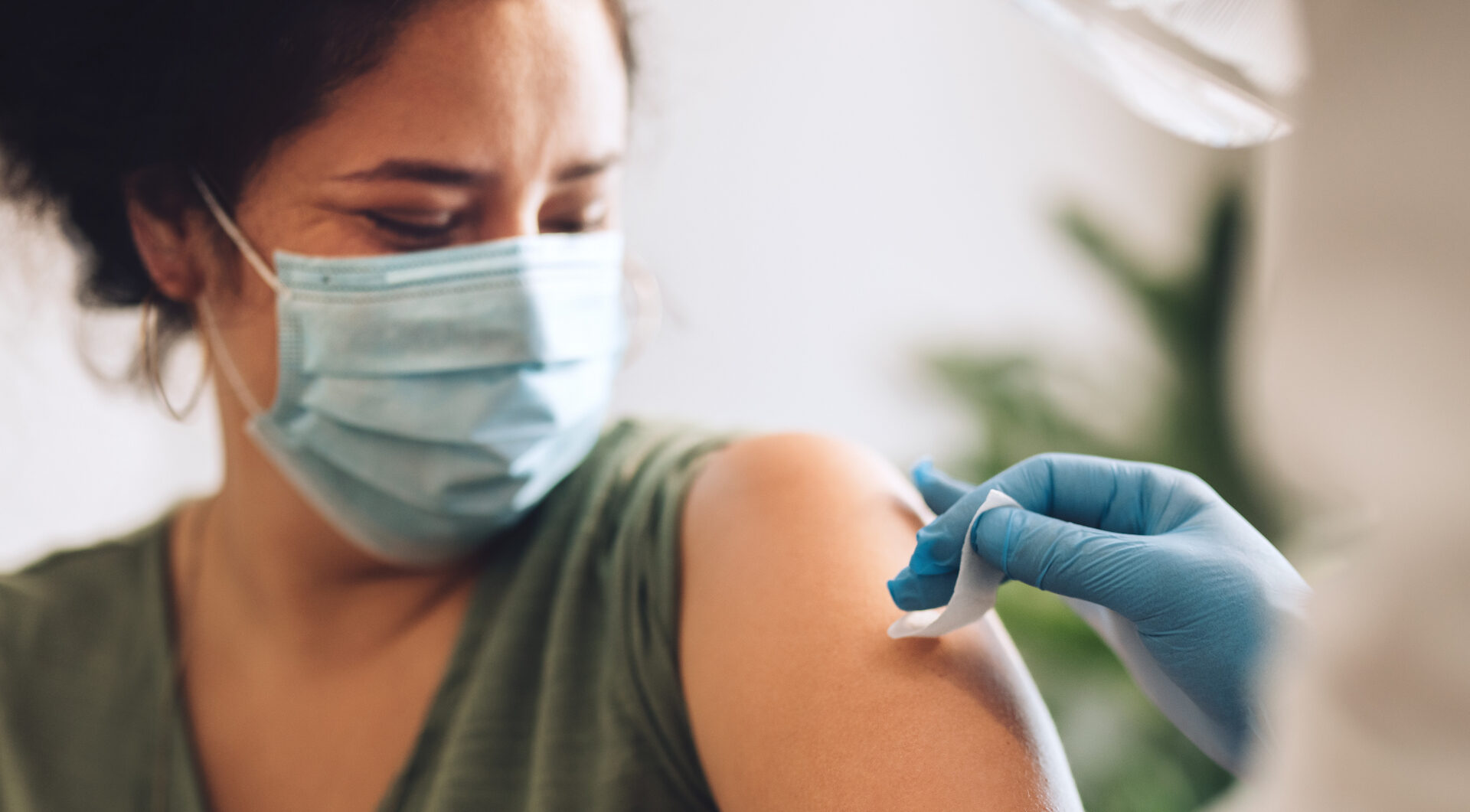 Woman wearing protective face mask getting vaccine shot at home. Female receiving covid vaccination by a healthcare worker at home.