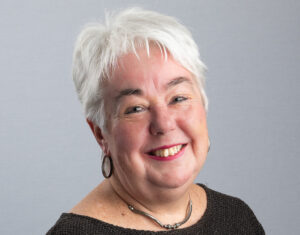 Dame au cheveux blancs courts sourit devant un fond gris