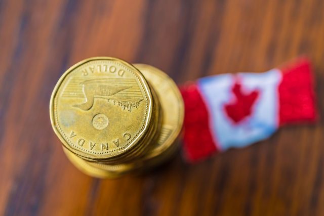 Stack of loonie coins on desk with canadian flag