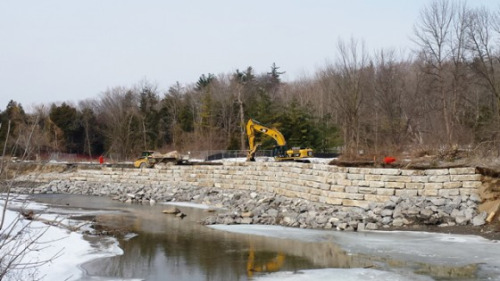 Backhoe adding material behind the wall
