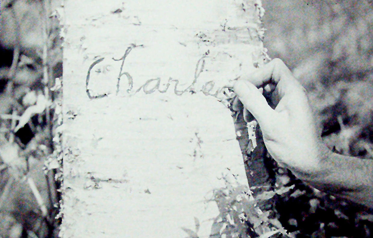 archival photograph of Charles Sauriol carving his name into a tree trunk