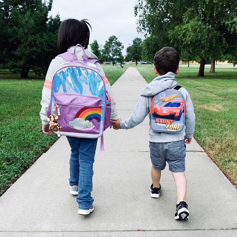 two children wearing knapsacks and walking hand in hand to school