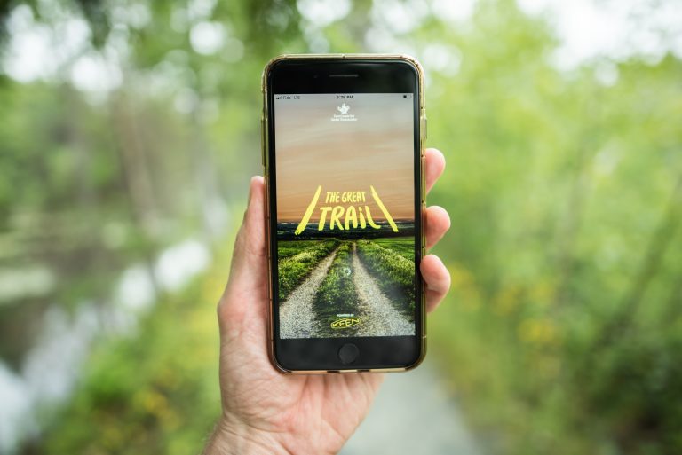 A person uses The Great Trail app on a trail surrounded by green trees in Nova Scotia.
